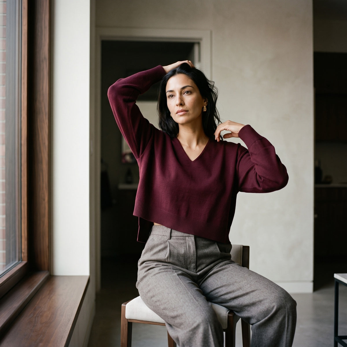 A woman wearing a Bordeaux V-neck sweater with grey tailored trousers