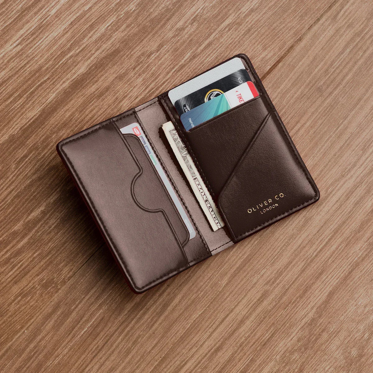 An open walnut-brown Oliver Co. compact wallet resting on a wooden surface