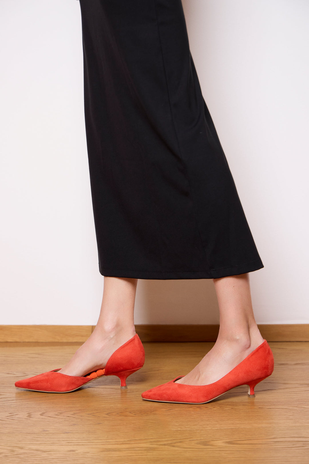 Model wearing AERA ARIANA orange kitten heel pumps with a black midi skirt.