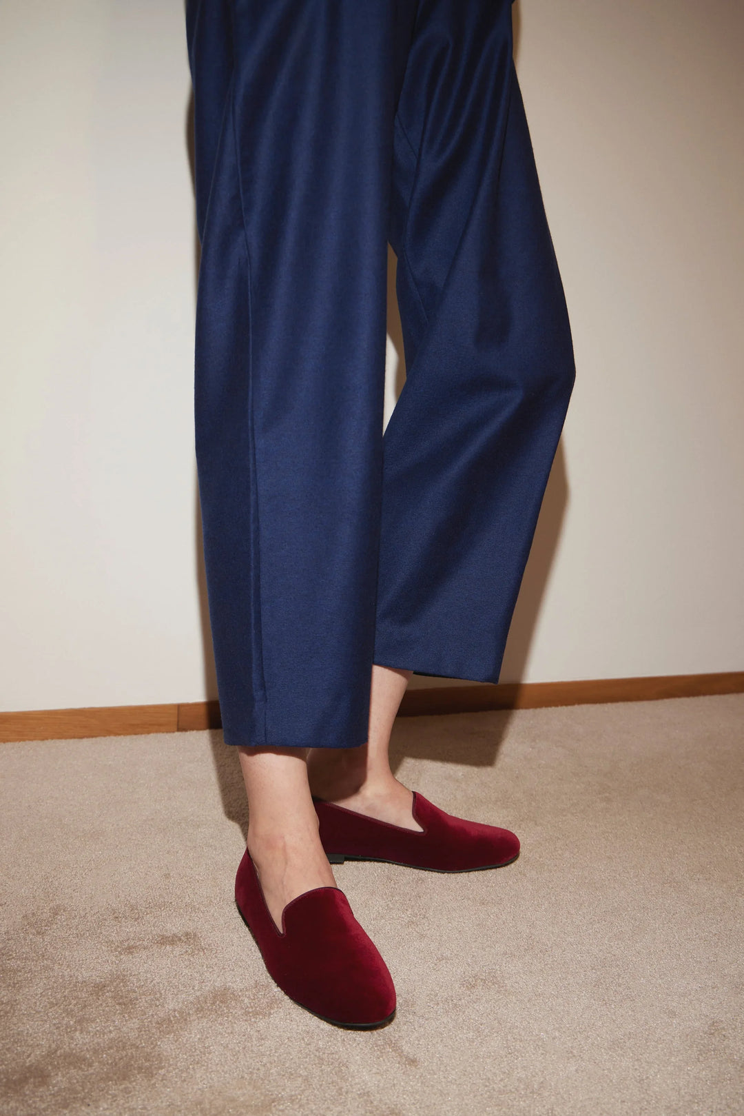 Person wearing wide-leg navy trousers and burgundy velvet loafers on beige carpet