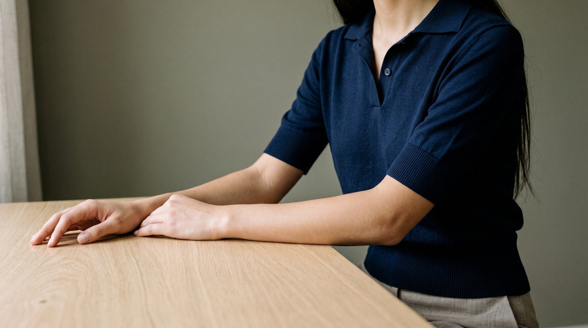 Mujer sentada ante una mesa de roble con un polo de punto de algodón azul marino.