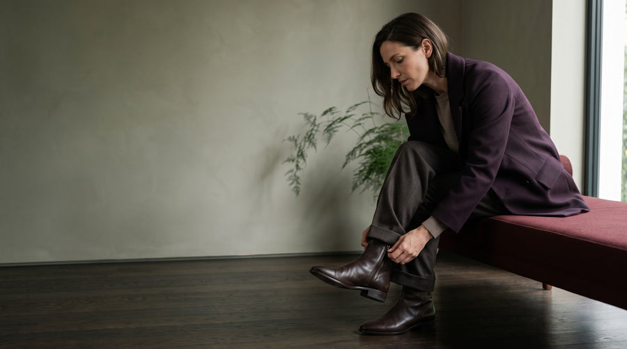 A woman in an aubergine jacket fastening her dark ankle boot